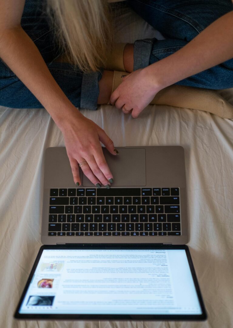 Teenage girl sitting on bed using laptop for online browsing or study in a cozy bedroom setting.